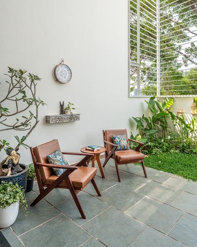 Two tan leather lounge chairs on a stone patio beside a lush garden with louvered wooden screen