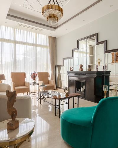 Living room with tiered mirrored fireplace surround, chandelier, and emerald velvet chair on marble floor