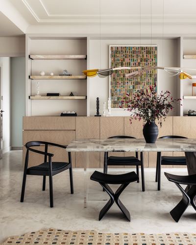 Dining area with marble table, black chairs, sculptural pendant light and framed artwork on shelving wall.