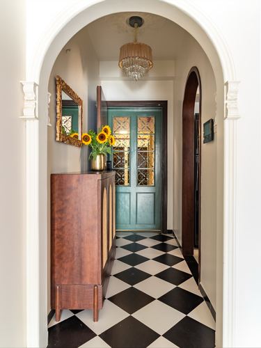 Arched foyer with checkerboard floor, cane cabinet, and view to teal jali door