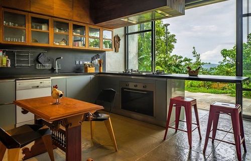 L-shaped kitchen with dark counters, wood cabinets, and glass wall overlooking greenery