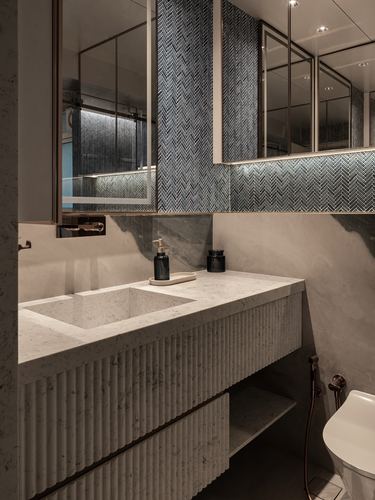 Bathroom with fluted marble vanity, undermount sink, and backlit mirror cabinets with herringbone mosaic tile.