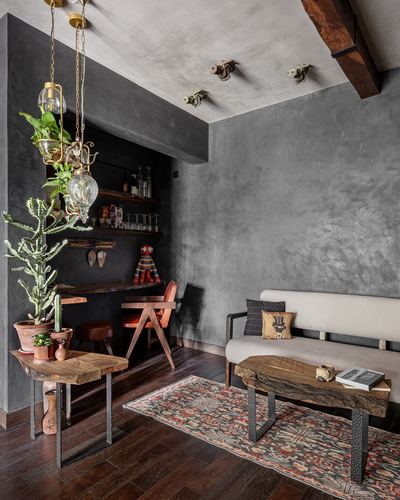 Grey plastered living room with bar nook, live-edge tables, patterned rug and beige sofa