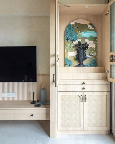 Wooden cabinet unit with arched painted mural niche housing a deity idol beside a wall-mounted tv