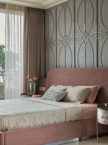 Bedroom with pink quilted headboard against a grey geometric-patterned wall panel and sheer curtains