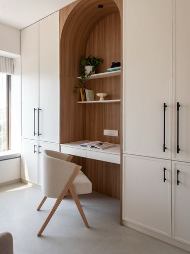 Arched wood-veneer study nook with shelves and desk built into cream wardrobes, wooden chair in front