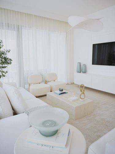 Neutral minimalist living room with sheer curtains, stone coffee table, and sculptural pendant light