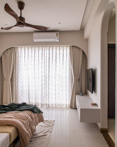 Bedroom with arched curtained window bay, wooden ceiling fan, and floating TV console in ivory tones
