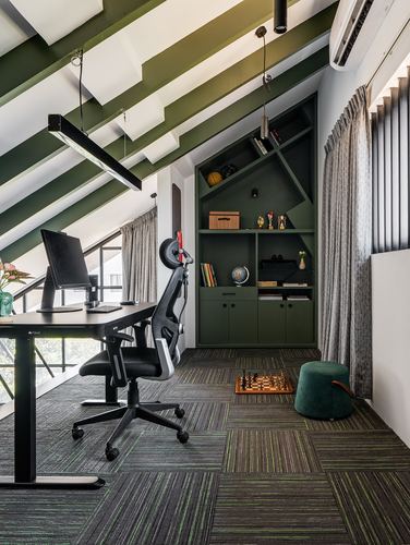 Attic home office with sloped green beam ceiling, black desk, and green built-in shelving