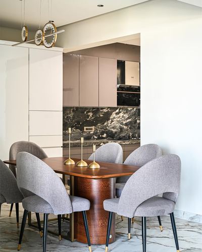 Dining table with grey curved chairs, brass candlesticks, dark stone kitchen backsplash beyond