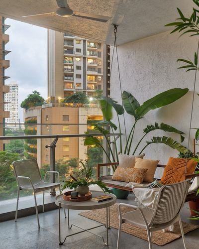 Balcony with hanging swing bench, cane chairs, plants, and Mumbai skyline view