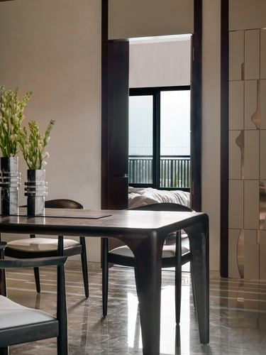 Dark sculpted wood dining table with marble vases, framed view through door to balcony