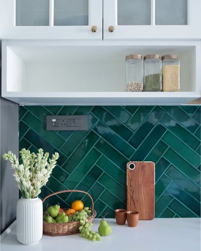 Kitchen counter with green herringbone tile backsplash, glass storage jars, fruit basket and vase of flowers