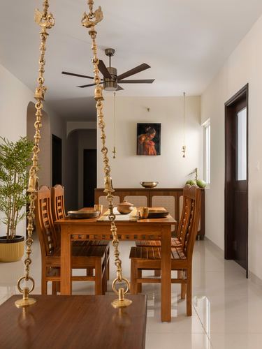 Dining room with wooden table, teak chairs, and decorative brass swing chains hanging from ceiling