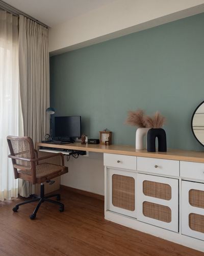 Home study with sage green wall, wooden floating desk, cane chair, and cane-front cabinets