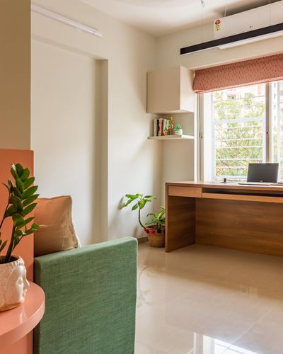 Home study nook with wooden desk under a window, green armchair and terracotta accents