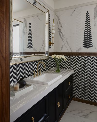 Bathroom vanity with black herringbone tile, marble walls with leaf motif, brass fittings