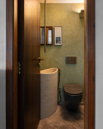 View through wooden door into olive-walled powder room with sculptural stone basin and black toilet
