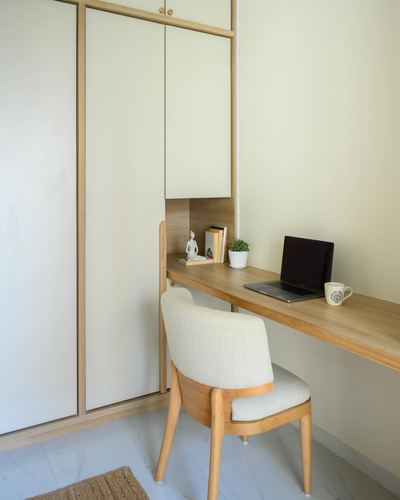 Wall-mounted wood desk with chair beside white built-in wardrobe in a Japandi study nook