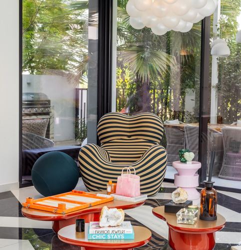 Striped armchair and orange lacquer coffee tables in a sunlit living corner with glass walls to garden