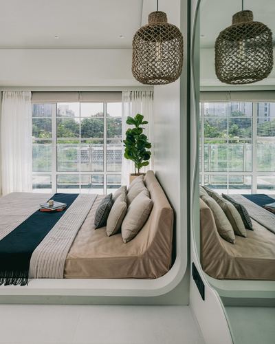 Curved beige bed platform beneath a woven pendant light beside floor-to-ceiling windows and mirrored wardrobe