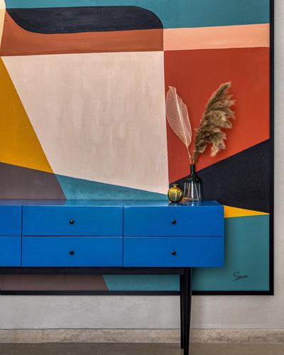 Glossy blue console table with black legs against a large geometric abstract painting