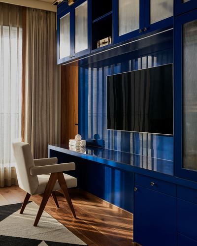 Navy lacquered built-in desk and TV cabinet beside a cane-backed armchair and sheer curtains