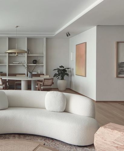 Curved white boucle sofa in open living space with dining area and brass pendant light beyond