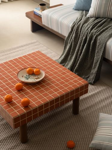 Terracotta tiled coffee table with fruit and ceramic plate beside striped sofa