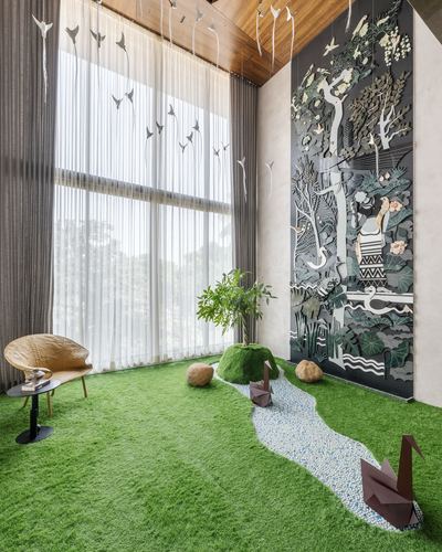 Triple-height living room with turf flooring, pebble path, origami swans, and large carved nature mural