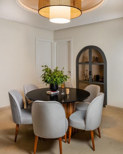 Round dark wood dining table with grey chairs beneath a woven drum pendant, arched display niche behind