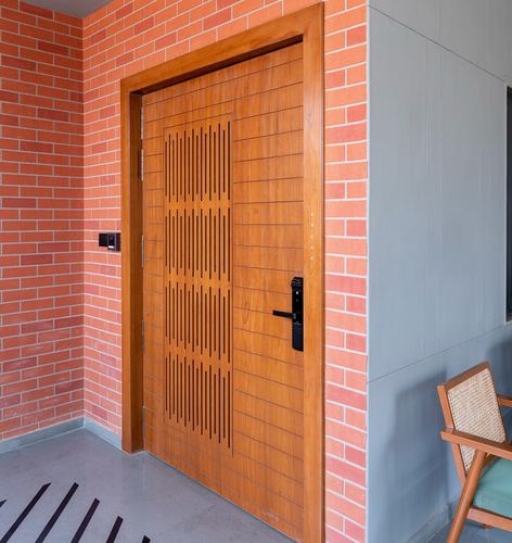 Wood entrance door with vertical slat carving set into a brick and concrete facade wall