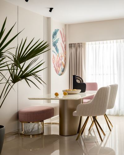 Dining nook with curved stone table, pink bench, quilted chairs and botanical wall art near sheer-curtained window
