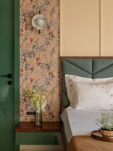 Bedroom corner with floral wallpaper, marble sconce, floating wood nightstand and green quilted headboard