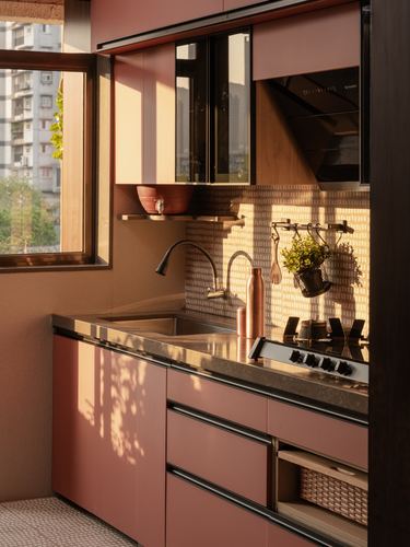 Blush pink kitchen corner with stainless counter, gas stove and sunlit window casting shadows