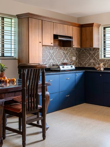 Kitchen corner with wood overhead cabinets, navy lower cabinets, patterned tile backsplash and carved wooden chair