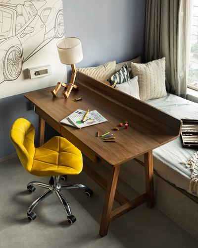 Wooden study desk with yellow velvet chair beside a daybed under a grey wall with a car sketch mural