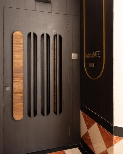 Dark wood entrance door with vertical carved cutouts beside a diamond-patterned marble floor