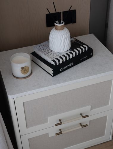 Nightstand corner with candle, diffuser, and stacked books on stone-top drawer unit