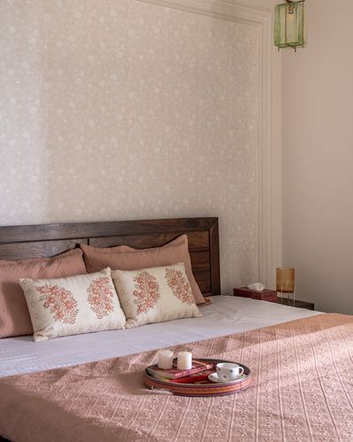 Bedroom with wooden headboard, blush bedding, embroidered cushions, and a decorative tray with candles