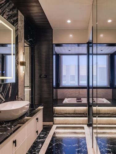 Dark marble bathroom with vessel sink, ribbed panelling, backlit mirror and window-side sunken tub