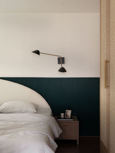 Bedroom corner with dark green fluted headboard wall and articulated brass wall sconce above nightstand