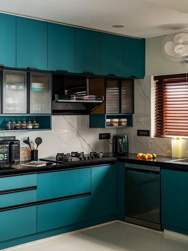 Teal L-shaped kitchen with black countertop, marble-look backsplash, gas hob and wooden window blinds