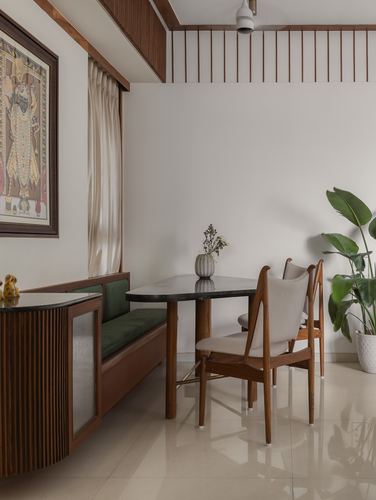 Dining nook with green velvet bench, marble-top table, wood chairs and framed painting
