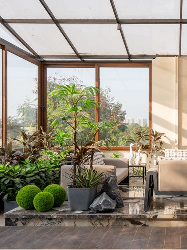 Sunroom seating area with potted plants, moss balls, and rocks on a stone ledge before large windows