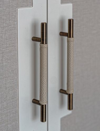 Close-up of two brass and leather-wrapped cabinet handles on textured wardrobe doors