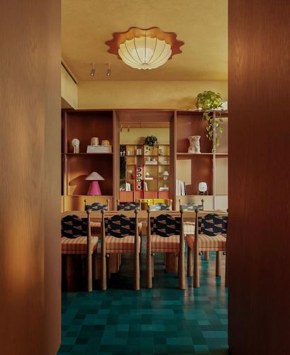 View through wooden doorway into ochre dining room with teal tiled floor and scalloped ceiling light
