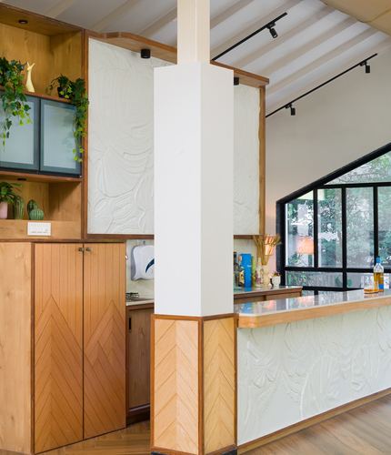 Kitchen bar area with chevron wood cabinetry, textured plaster panels, and a central column under a slanted skylight ceiling
