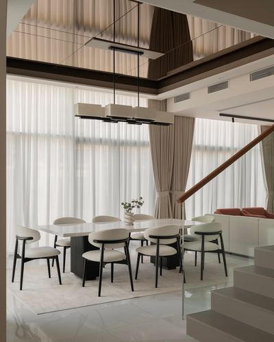 Double-height dining room with sheer curtains, stone-top table, cane-detailed base, and reflective ceiling