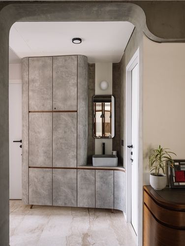 Arched doorway framing curved concrete-finish cabinetry leading to a small vanity nook